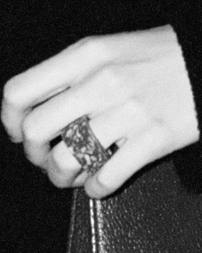 Une main portant une large bague tient une bouteille contre une étoffe sombre