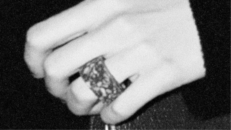 Une main portant une bague se détache sur un fond sombre
