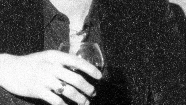 Une main tient un verre de vin devant une veste sombre